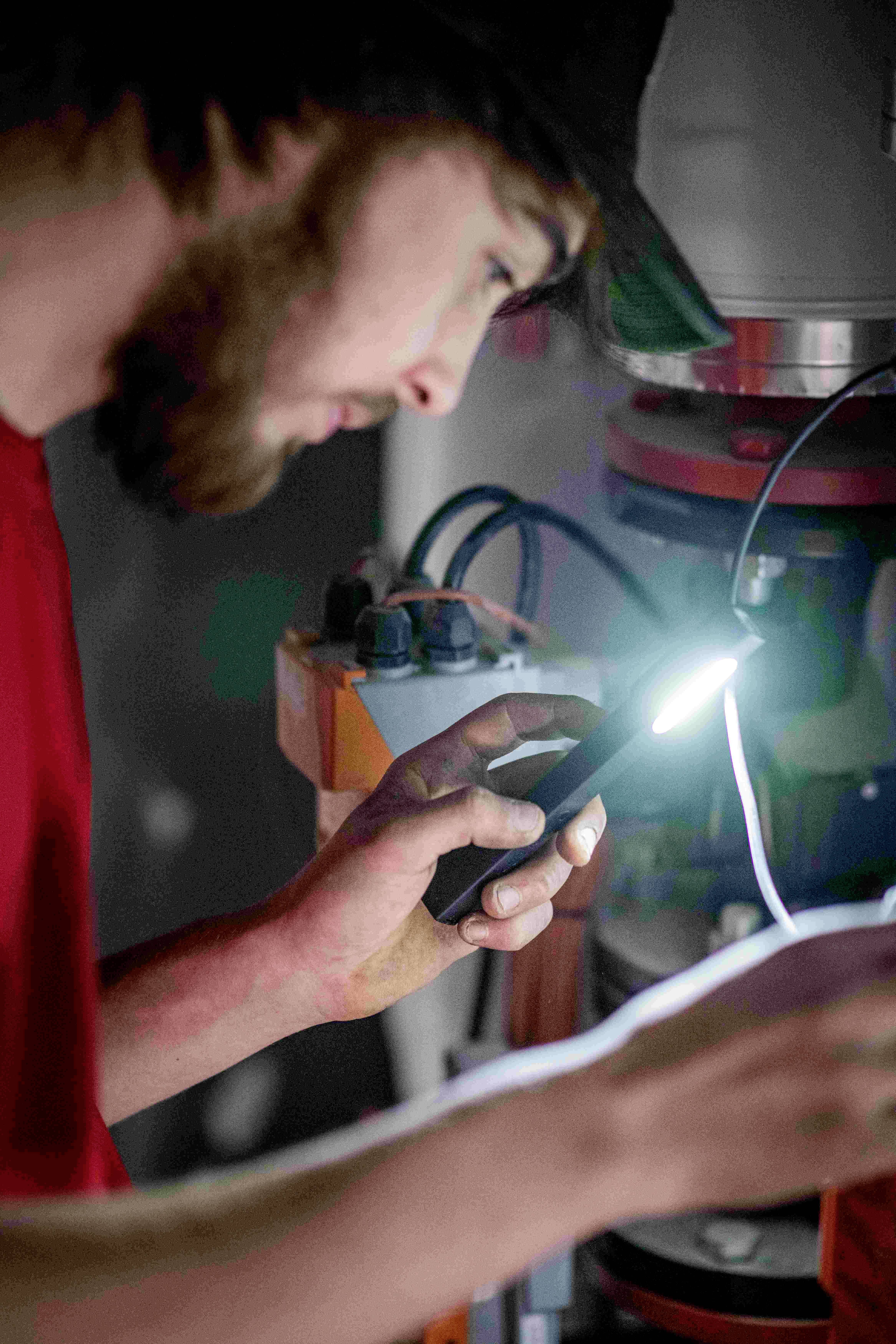 Un homme utilise une lampe torche pour inspecter des composants électriques dans un appareil. Il se concentre sur son travail.