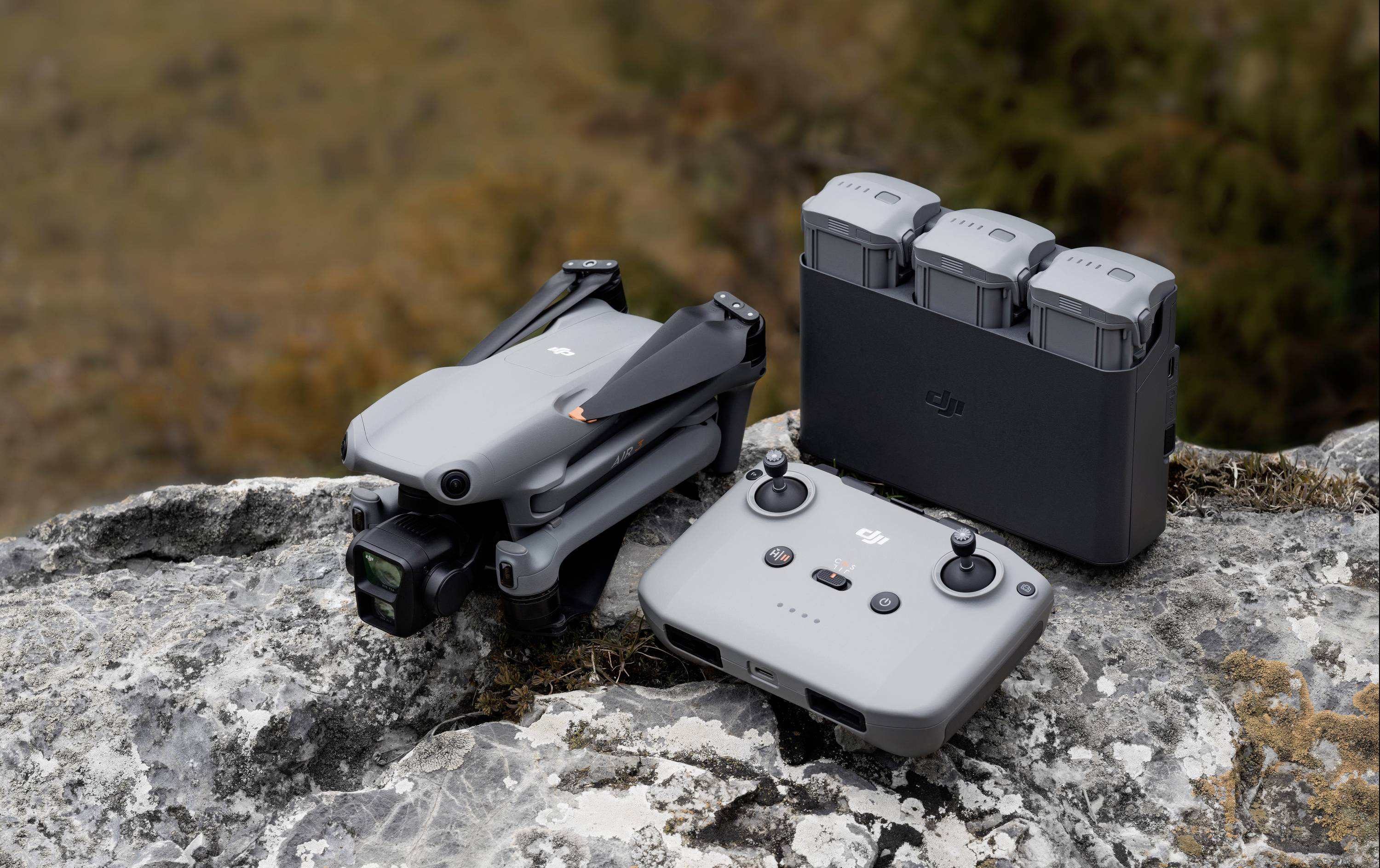 'Drone grise sur un rocher avec télécommande et étui de batterie. Arrière-plan flou aux couleurs naturelles.'