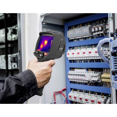 Une main tient une caméra thermique devant un armoire électrique ouverte. Sur l'écran, des différences de température sont visibles.