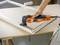Une personne utilise un outil électrique orange pour enlever la peinture d'un vieux cadre de fenêtre posé sur une table.