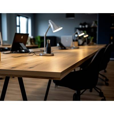 Un espace de bureau moderne et vide avec une longue table en bois, sur laquelle sont posées trois lampes de bureau et des ordinateurs portables. À l'arrière-plan, de grandes fenêtres.