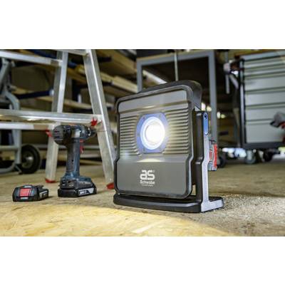 Chantier avec une lampe de travail, une perceuse et des batteries au sol ; des étagères et des outils en arrière-plan.