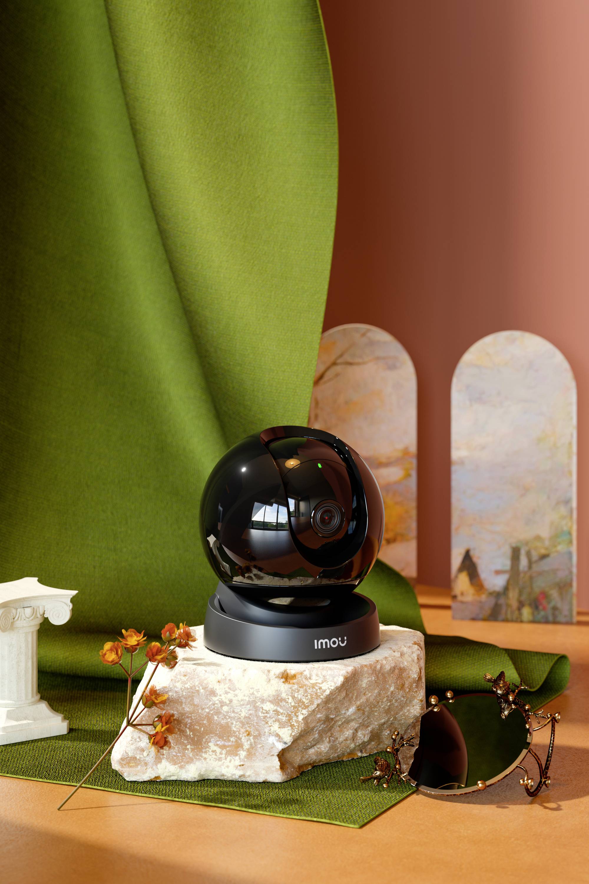 Une caméra de sécurité noire de forme sphérique, installée sur un socle en marbre, entourée de décorations automnales et de tissus colorés.