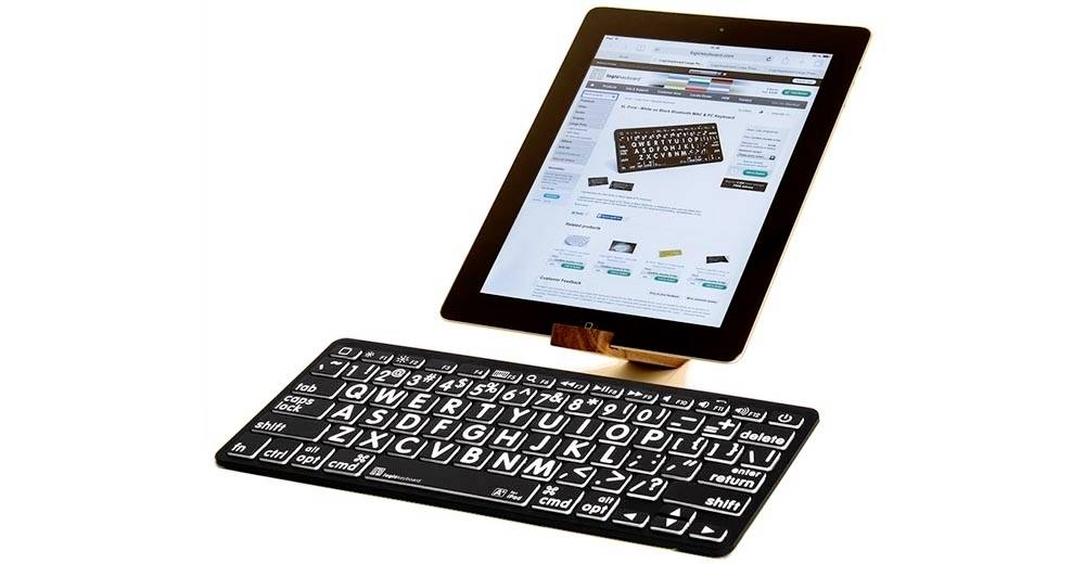Une tablette sur support affiche un site web proposant des claviers. Un clavier physique est posé devant la tablette, prêt à être utilisé.