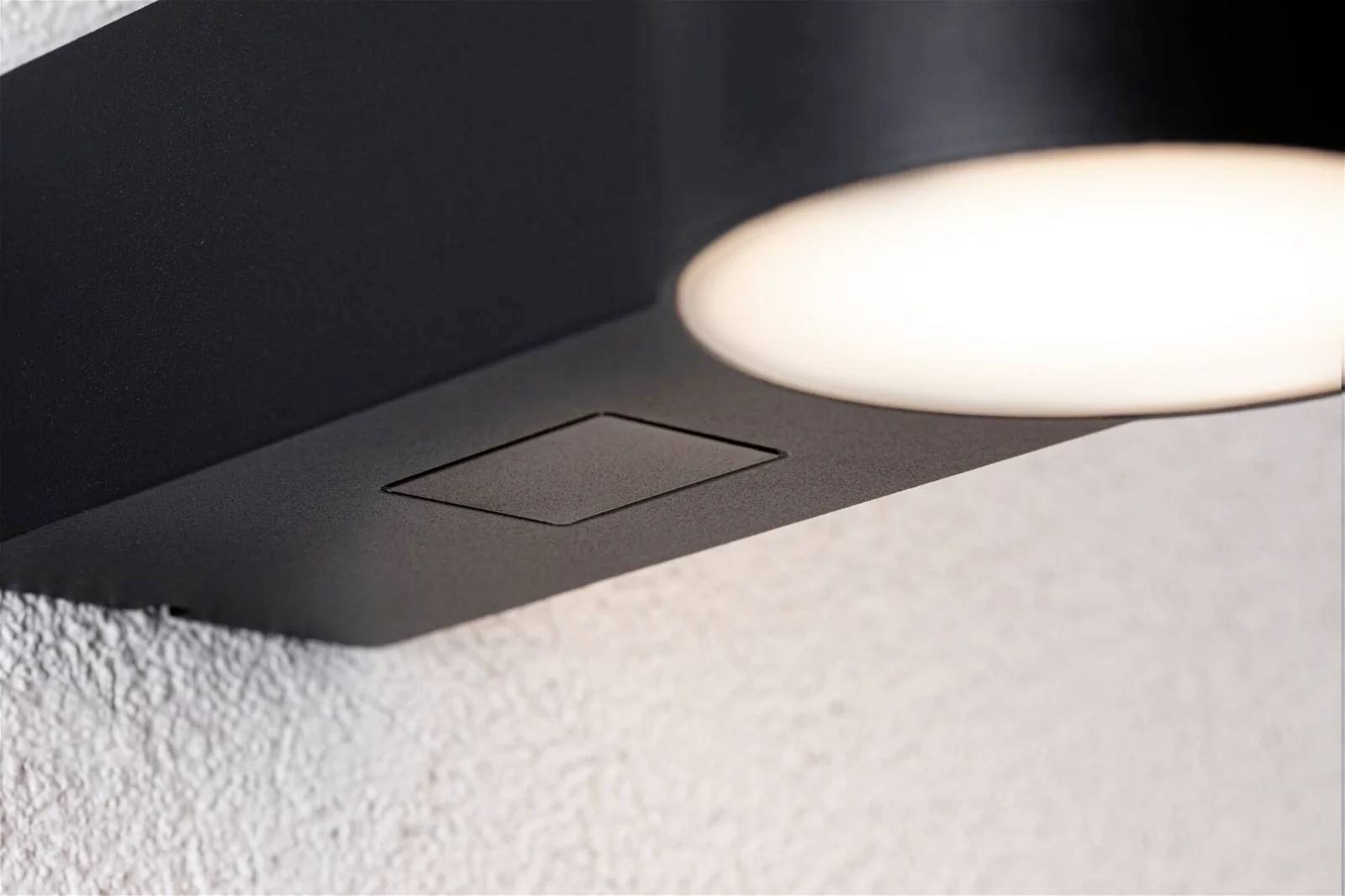 Un luminaire de plafond moderne et rond avec un boîtier noir, monté sur un mur blanc, éclaire uniformément la pièce.