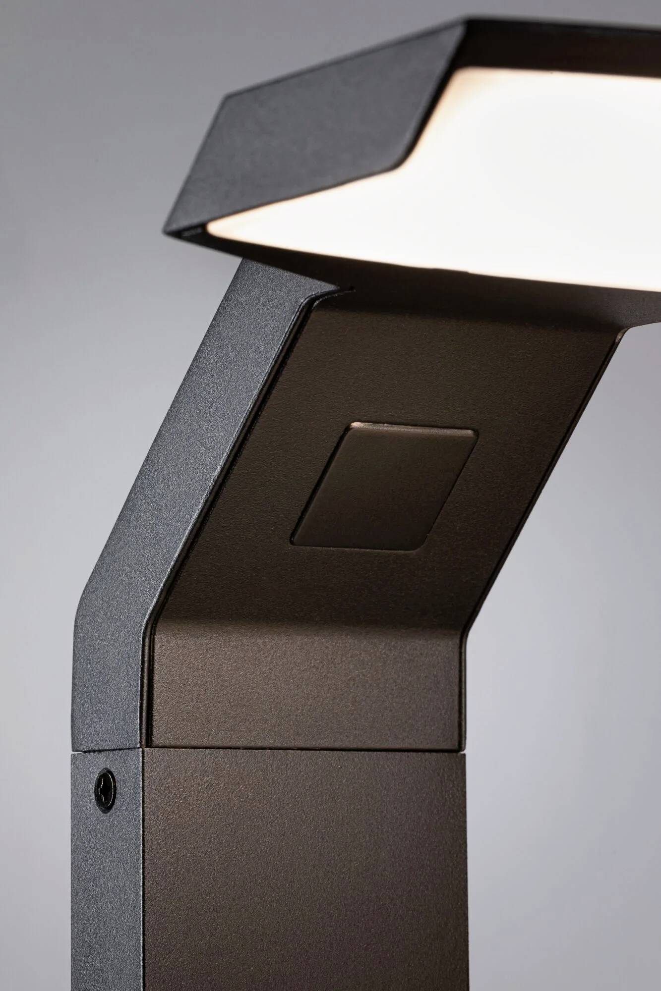 Lampe d'extérieur moderne noire au design épuré, avec une tête rectangulaire dirigeant la lumière vers le bas. Conception minimaliste pour espaces extérieurs.