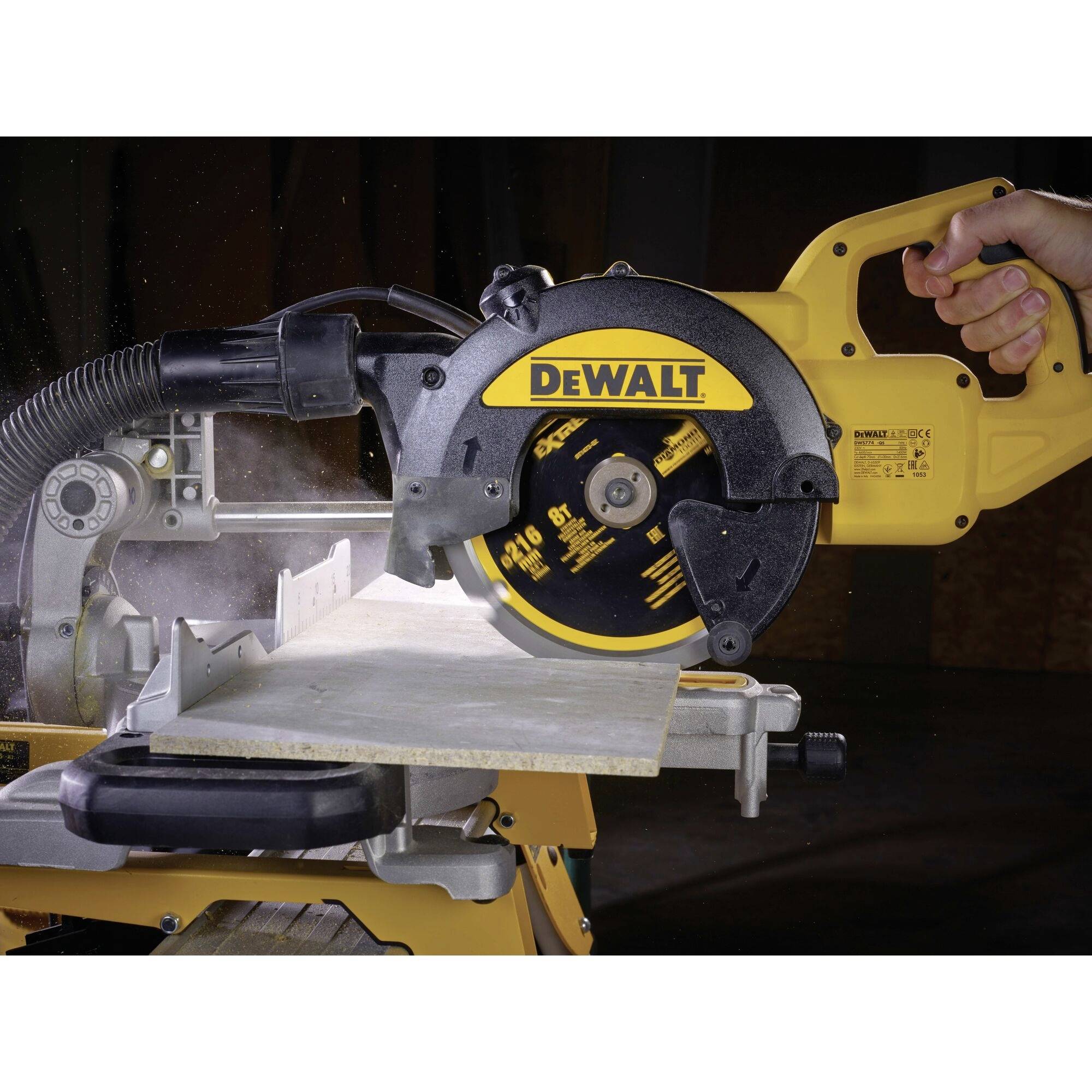 Une main tient une scie circulaire électrique jaune de la marque DeWalt, qui coupe à travers une planche en bois. La poussière est aspirée.