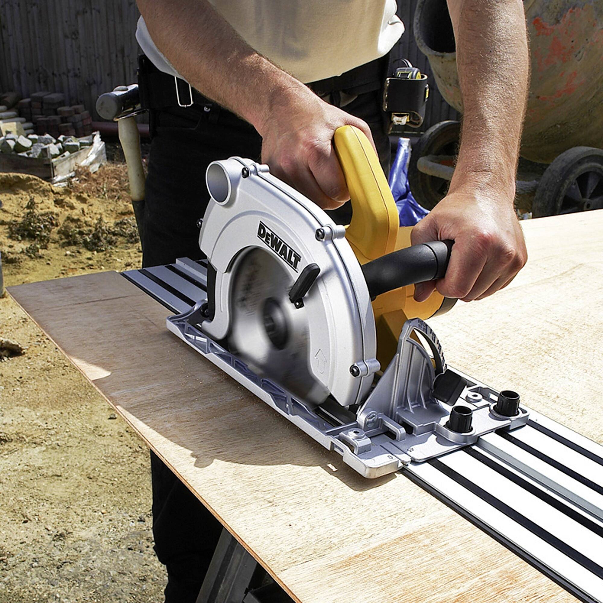 Une personne coupe une planche en bois avec une scie circulaire manuelle sur un chantier de construction. La scie a une poignée jaune et glisse sur un rail de guidage.