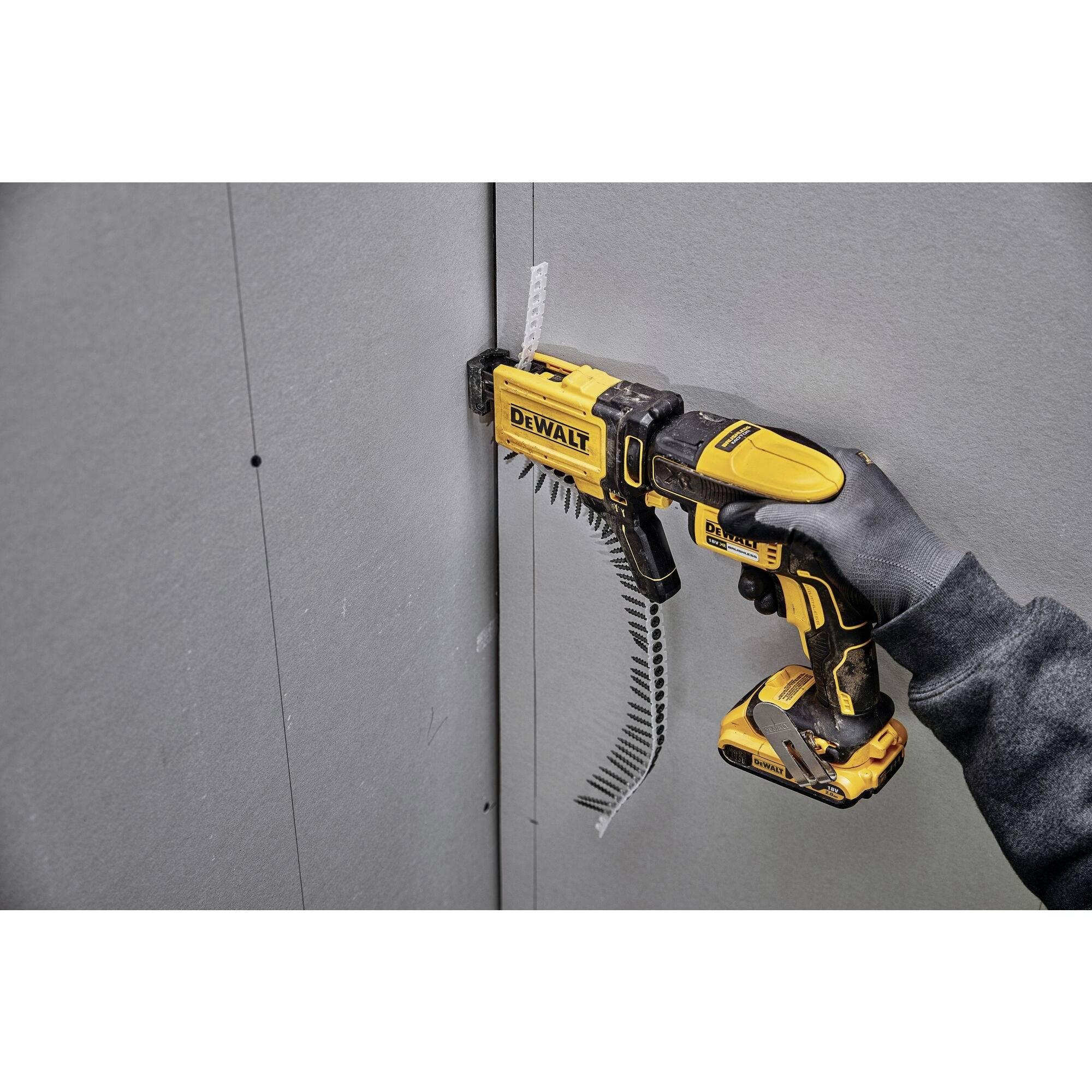 Une personne utilise une visseuse jaune pour visser une vis dans un mur de plaque de plâtre gris.