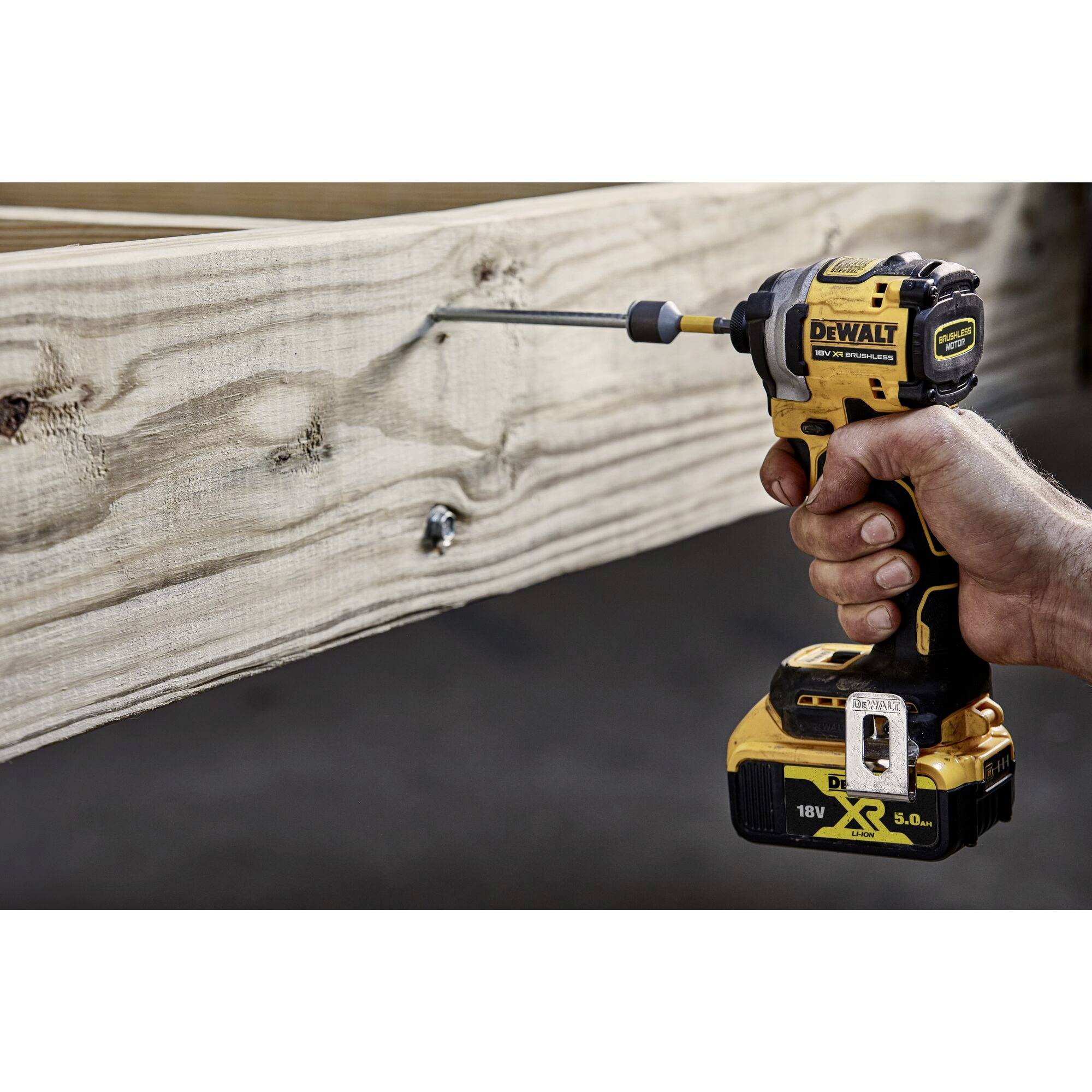 Une personne utilise une visseuse à chocs sans fil DEWALT pour visser une longue vis dans une poutre en bois.