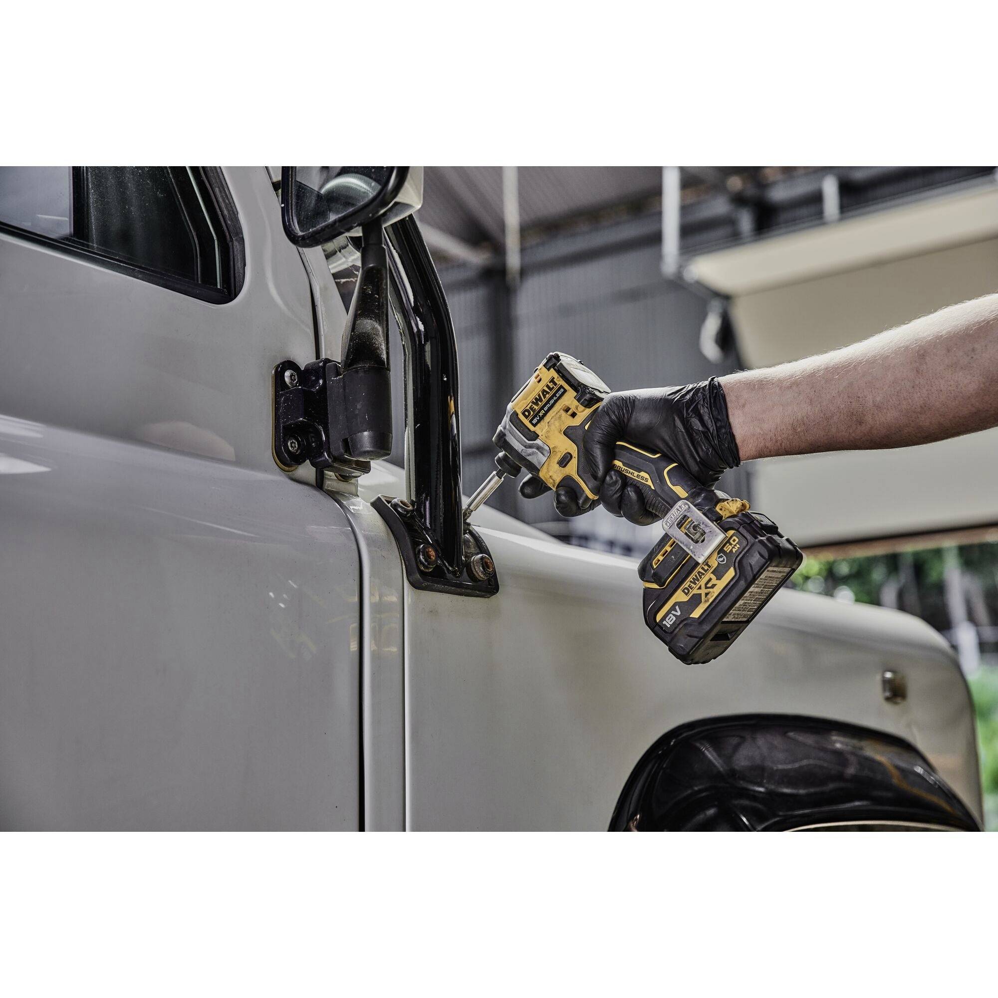 Une personne répare un rétroviseur de voiture avec un tournevis électrique. Elle porte des gants noirs.