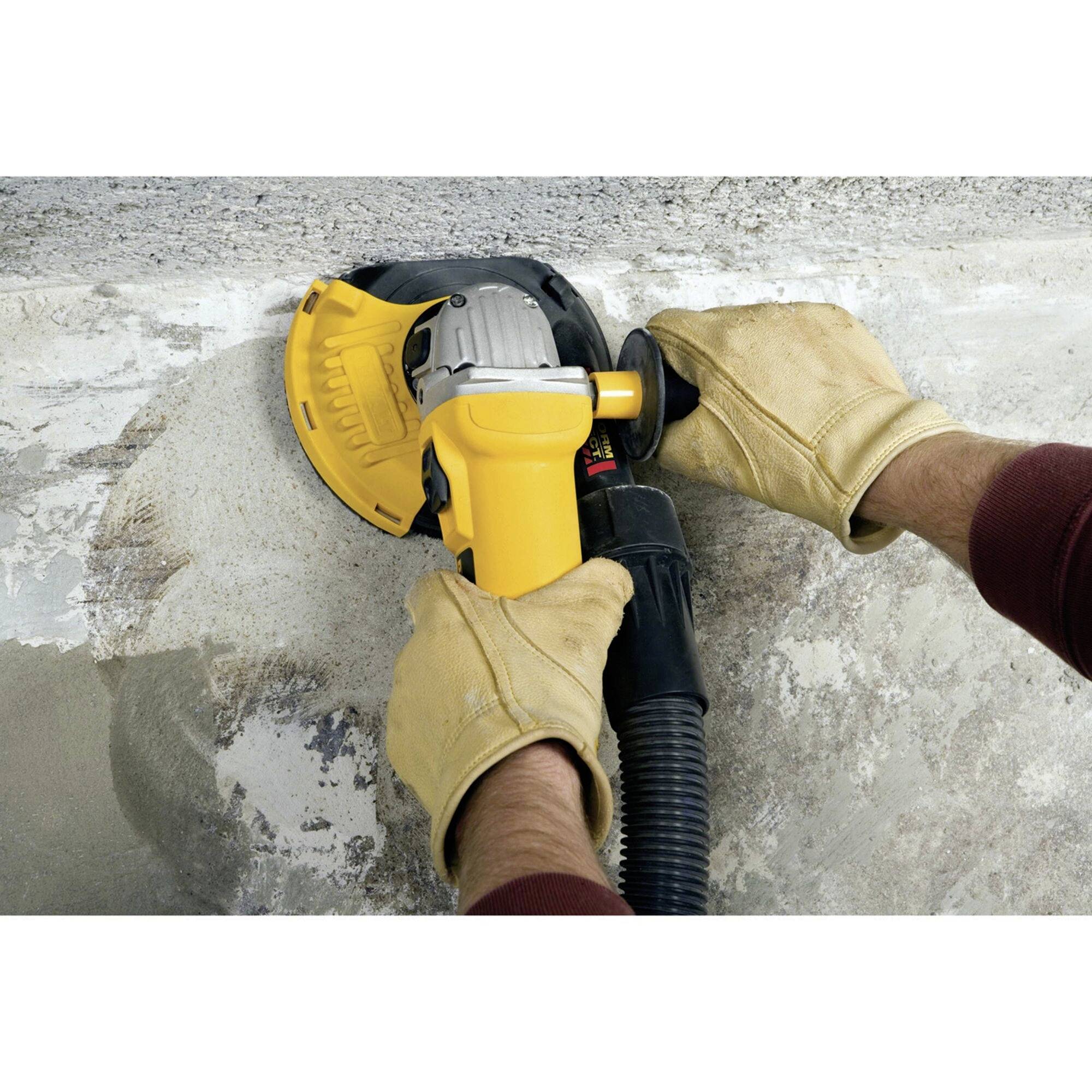 Une personne ponce une surface en béton avec un meuleuse d'angle. Des gants protègent les mains pendant que la poussière est aspirée.