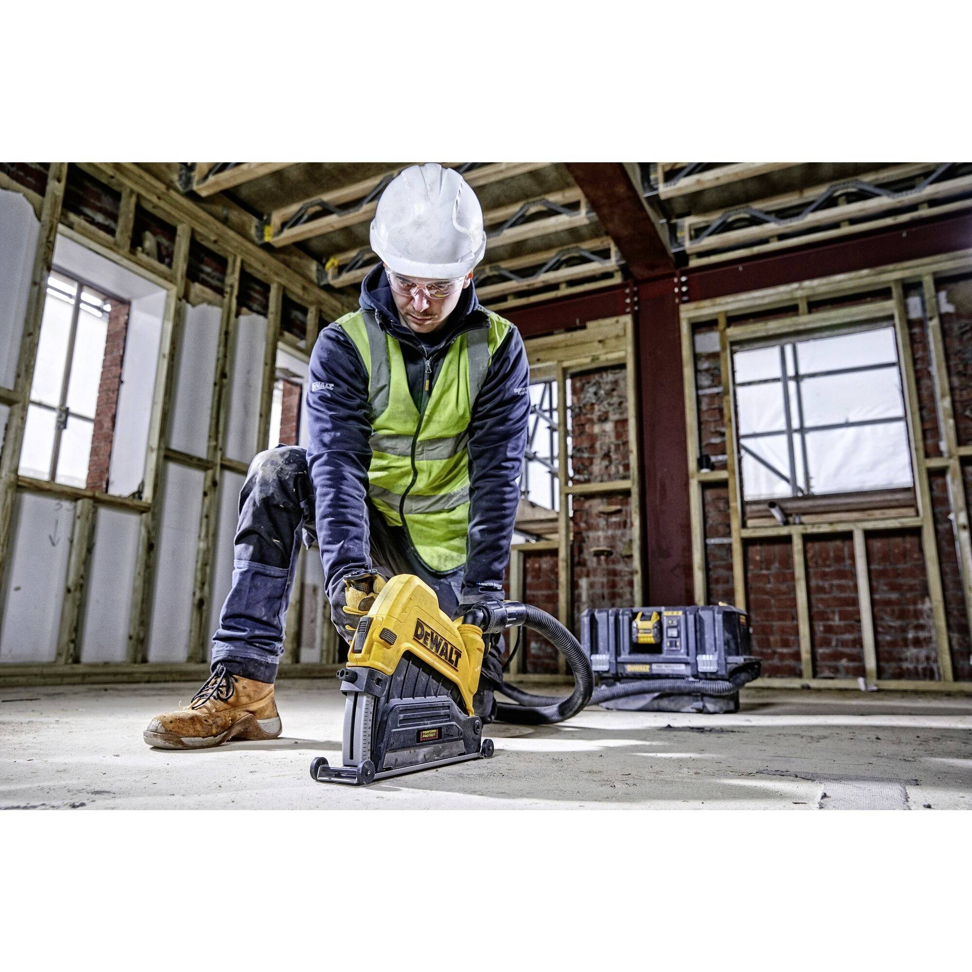 Un ouvrier en tenue de protection utilise un outil électrique dans une pièce inachevée avec un échafaudage en bois et des murs de briques bruts.