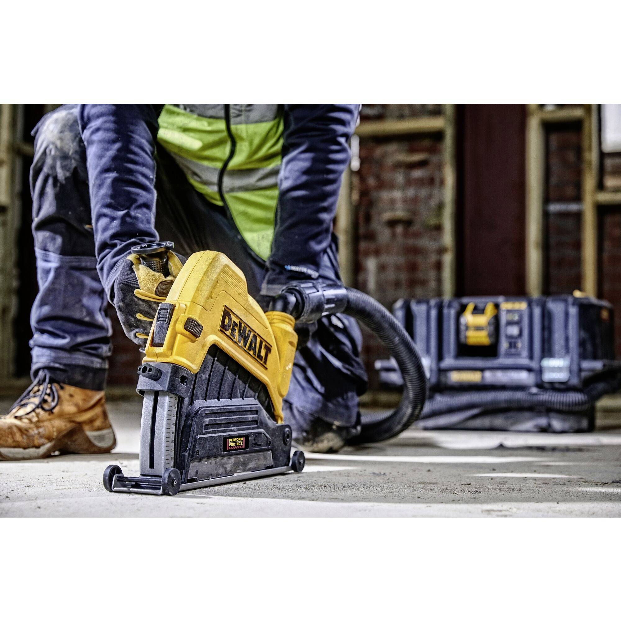 Une personne est agenouillée sur un sol en béton et travaille avec un outil électrique jaune, tandis qu'une boîte à outils est visible en arrière-plan.