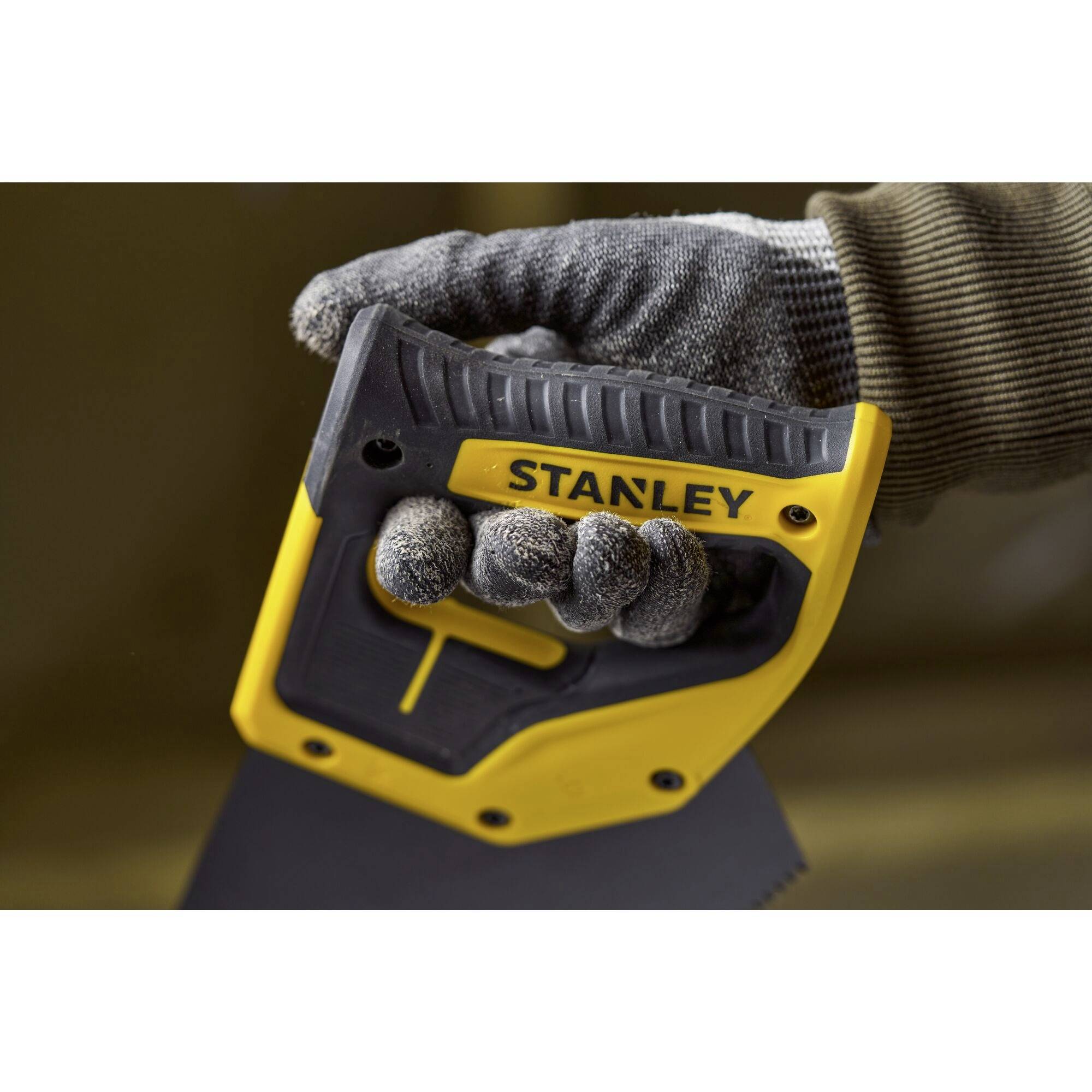 Une main gantée tient une scie jaune de la marque 'STANLEY', prête à scier une surface.