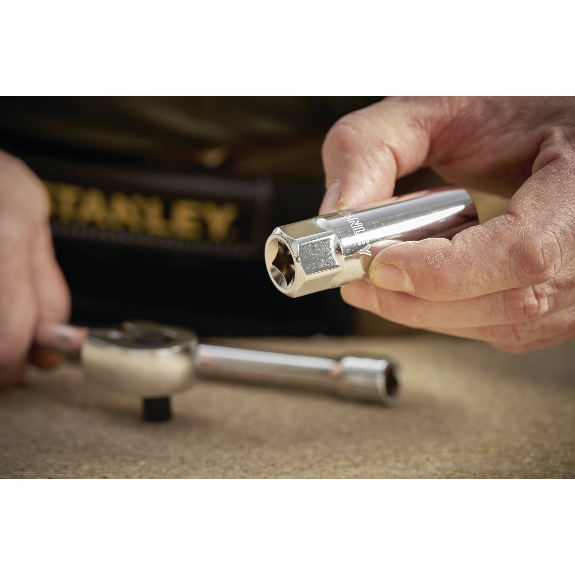 Gros plan de deux mains tenant un écrou, à côté d'une clé à douille sur une table en bois. Un coffret à outils est visible en arrière-plan.
