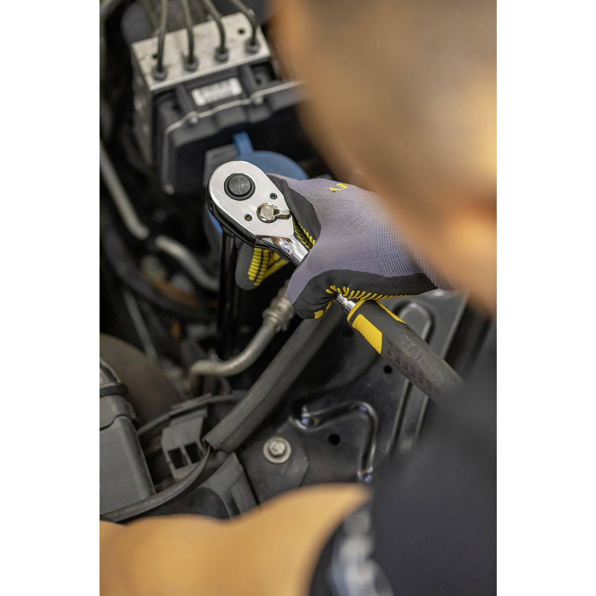 Une personne portant des gants répare ou effectue une maintenance avec une clé dynamométrique sur un moteur de véhicule ou une machine complexe.