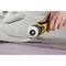 Une main utilise un cutter rotatif jaune pour suivre précisément un motif sur un tissu gris.