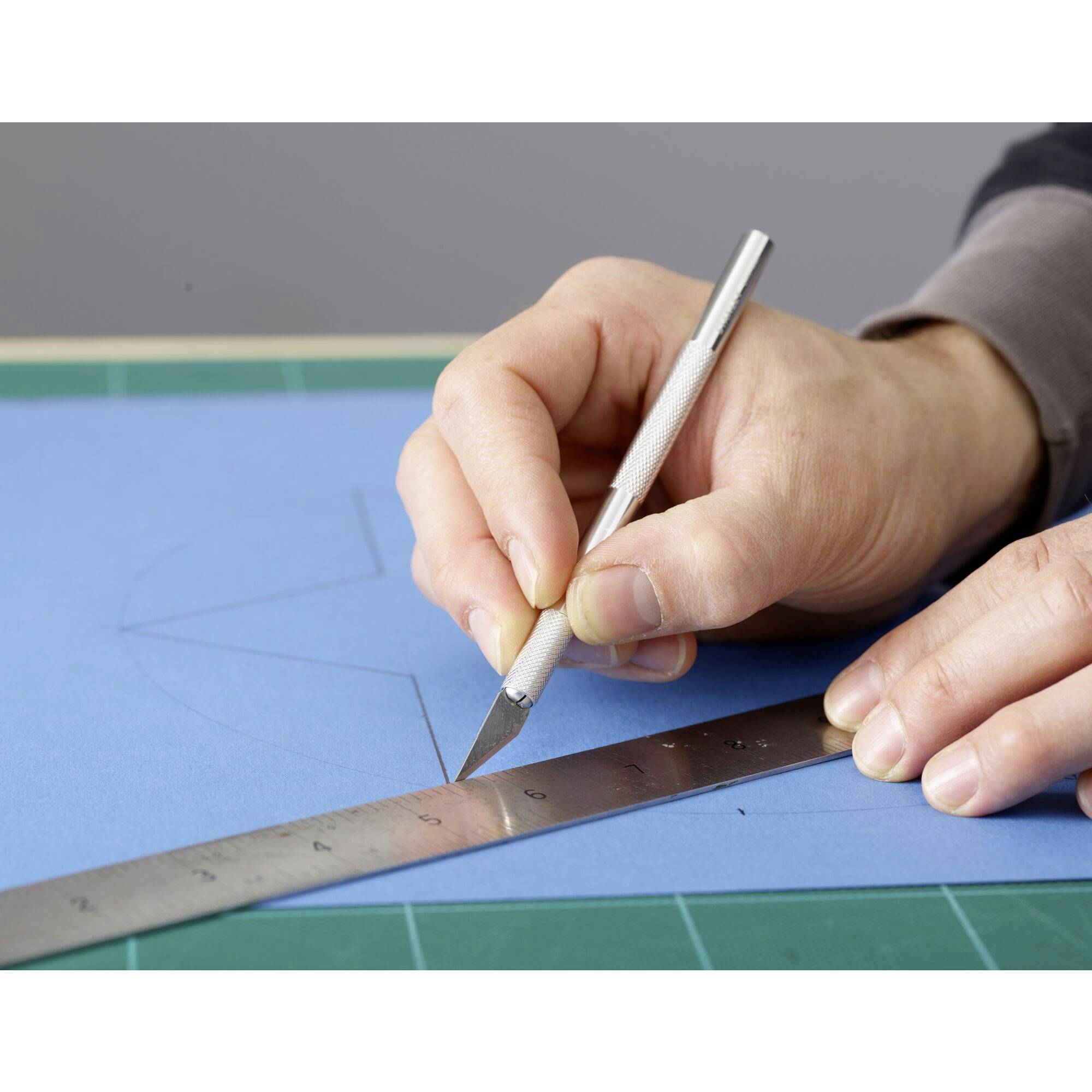 Une main coupe une ligne droite sur du carton bleu à l'aide d'un scalpel et d'une règle.