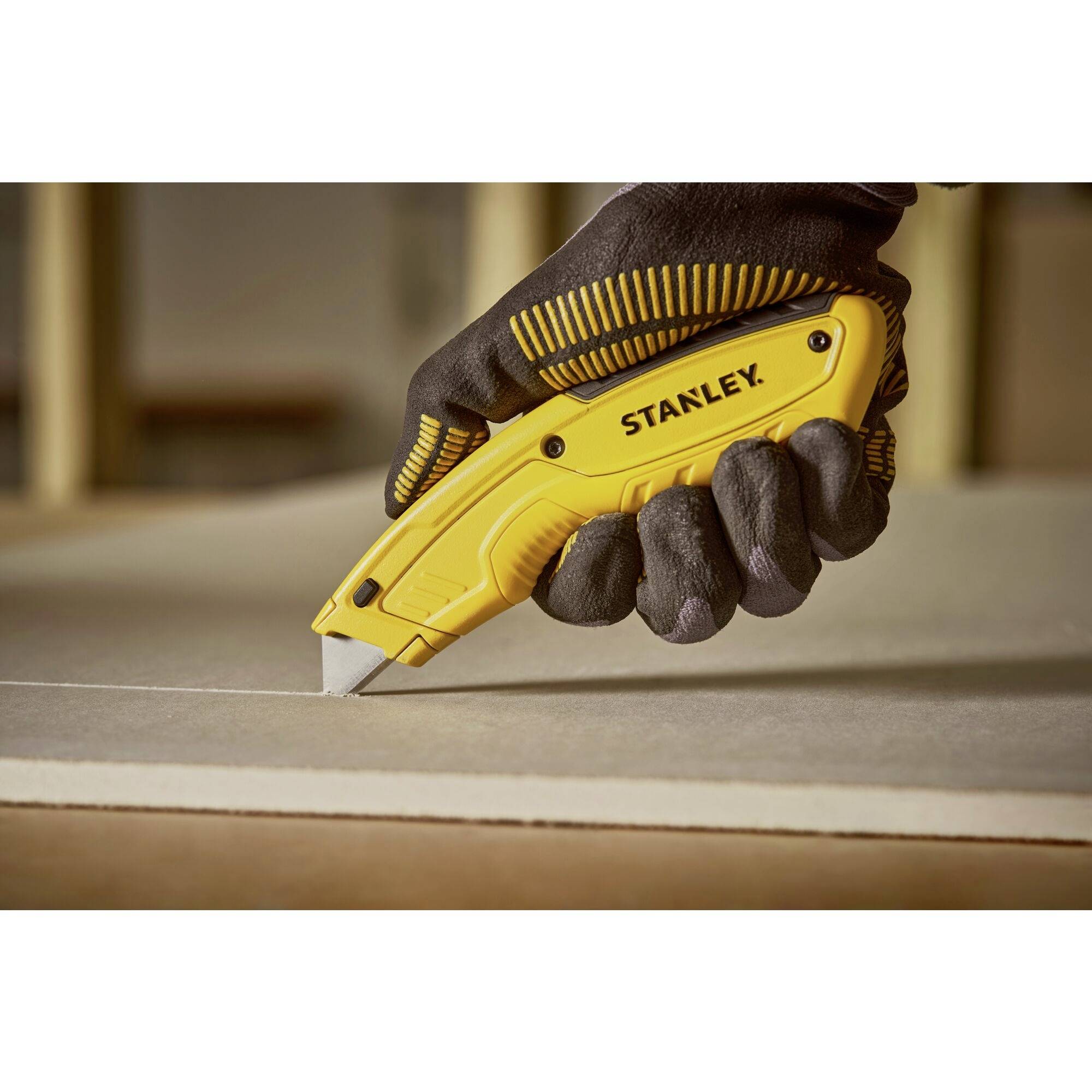 Une main gantée tient un couteau utilitaire Stanley jaune et coupe du carton.