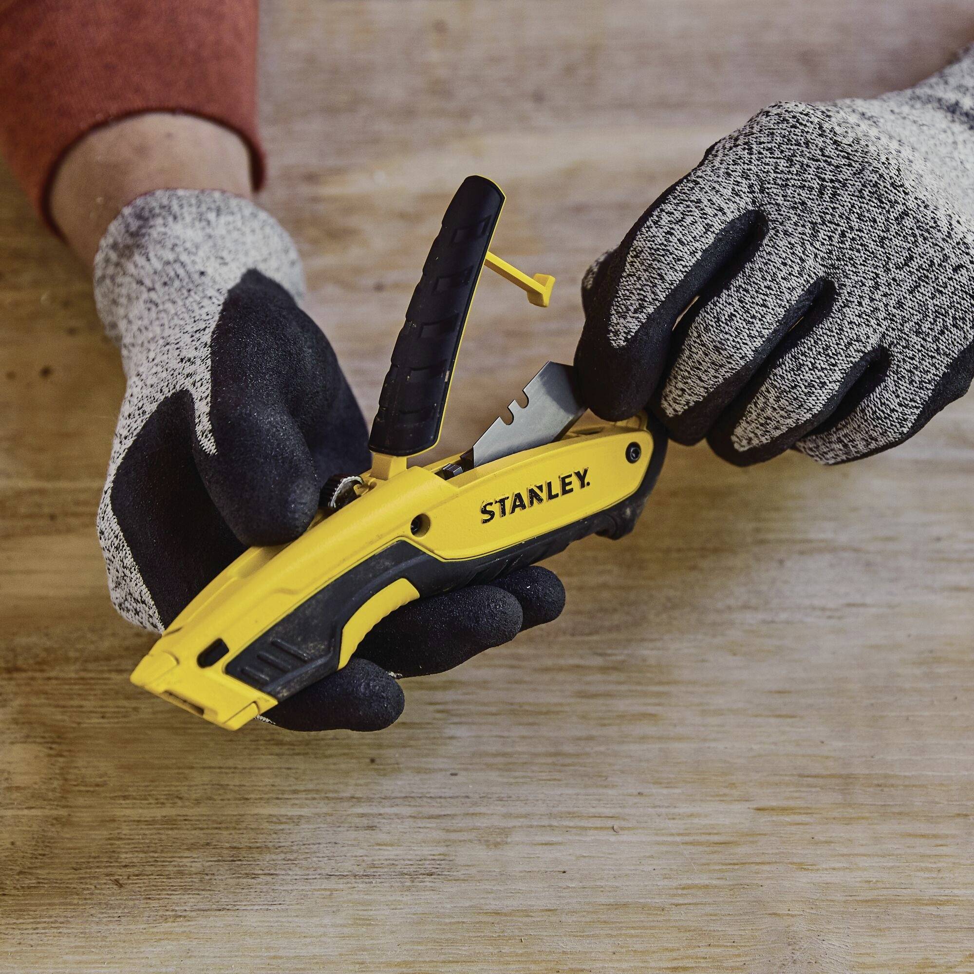 Une personne portant des gants manipule un outil jaune Stanley sur une surface en bois.