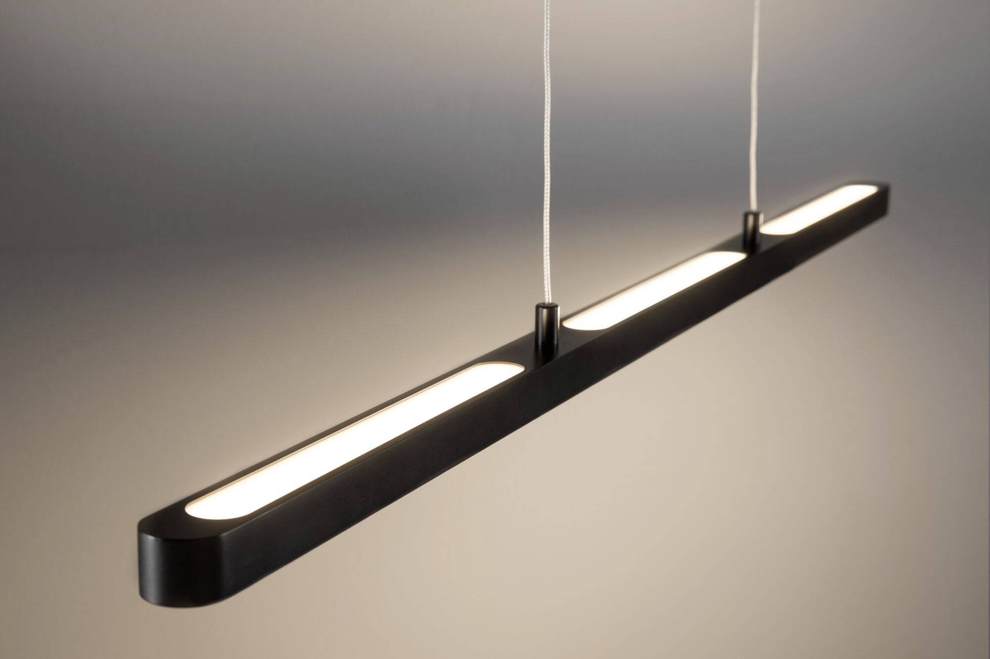 Un luminaire suspendu moderne, noir, doté de trois lumières réparties de manière uniforme et suspendues au plafond par de fins câbles.