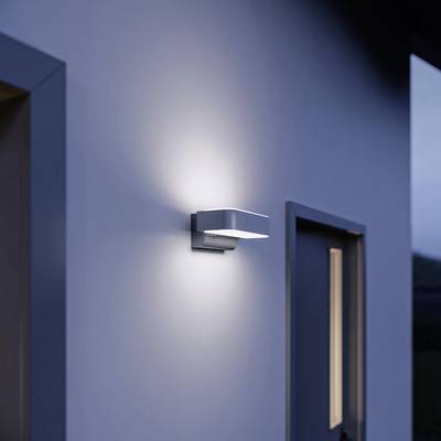 Applique murale moderne sur un mur blanc à côté d'une porte, éclairant vers le haut et vers le bas. Illumine la zone d'entrée la nuit.
