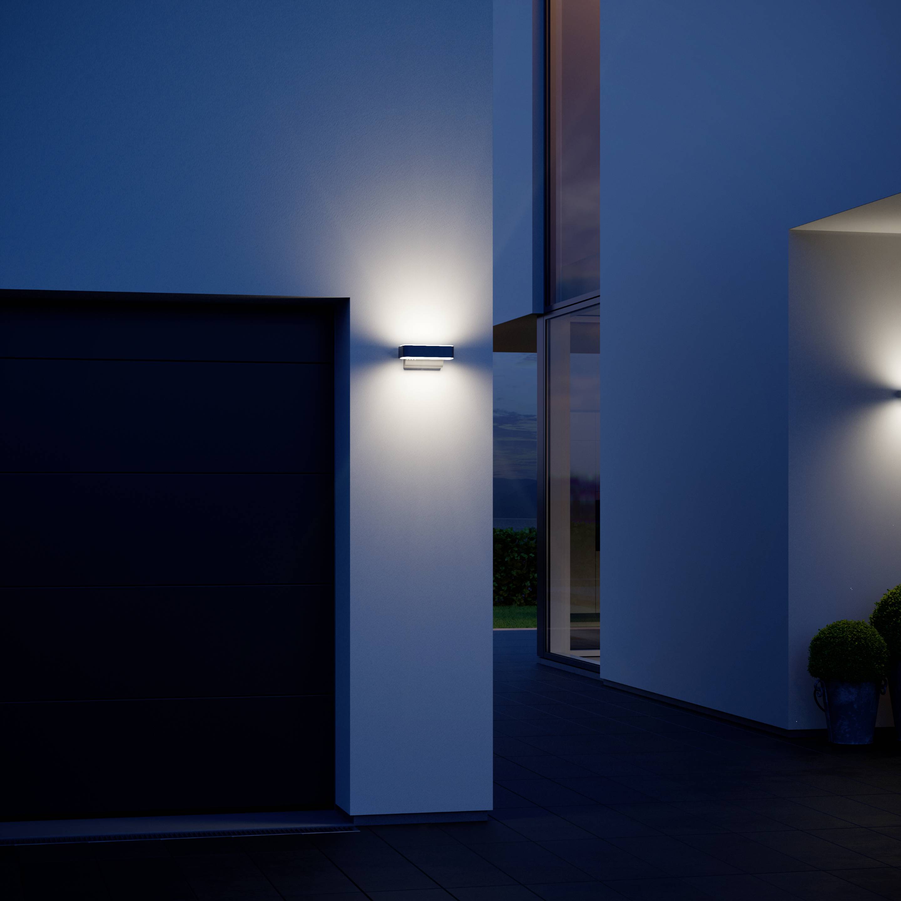 Une maison moderne au crépuscule avec façade extérieure éclairée et surface lisse de couleur grise. Un garage et un chemin piétonnier illuminé sont visibles.