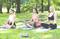 Trois femmes sont assises dehors sur des tapis de yoga, en position du tailleur, méditant dans un environnement qui ressemble à un parc.
