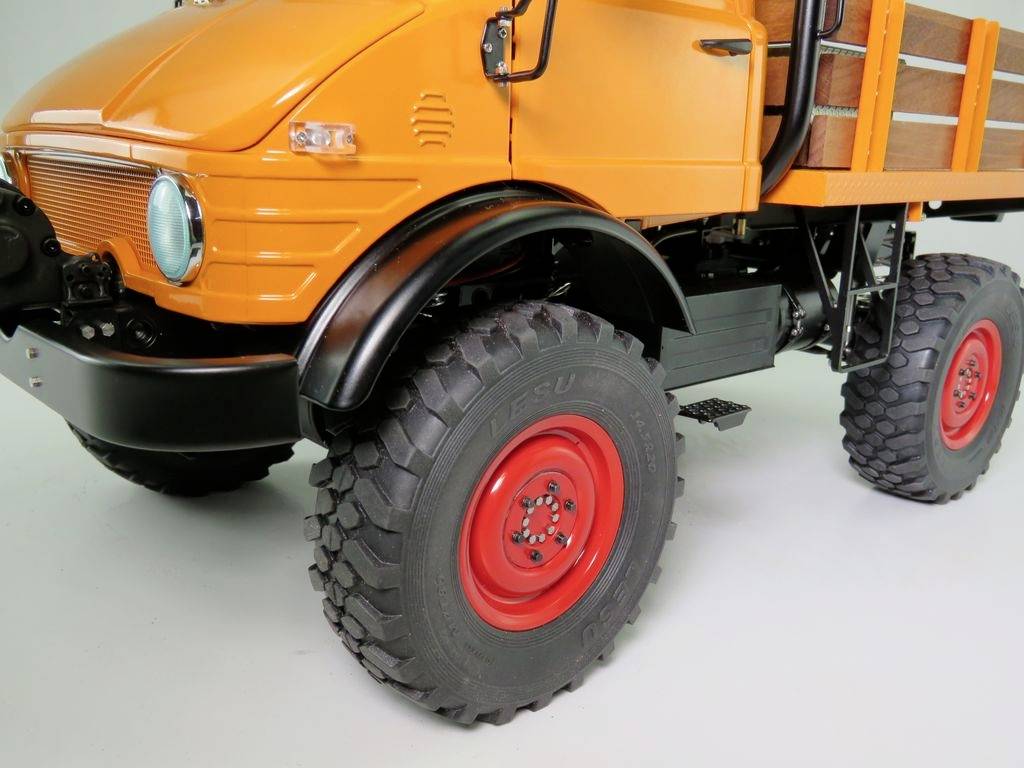 Un tout-terrain orange avec des roues rouge marquantes et un chargement de panneaux en bois. Robuste et adapté aux terrains difficiles.