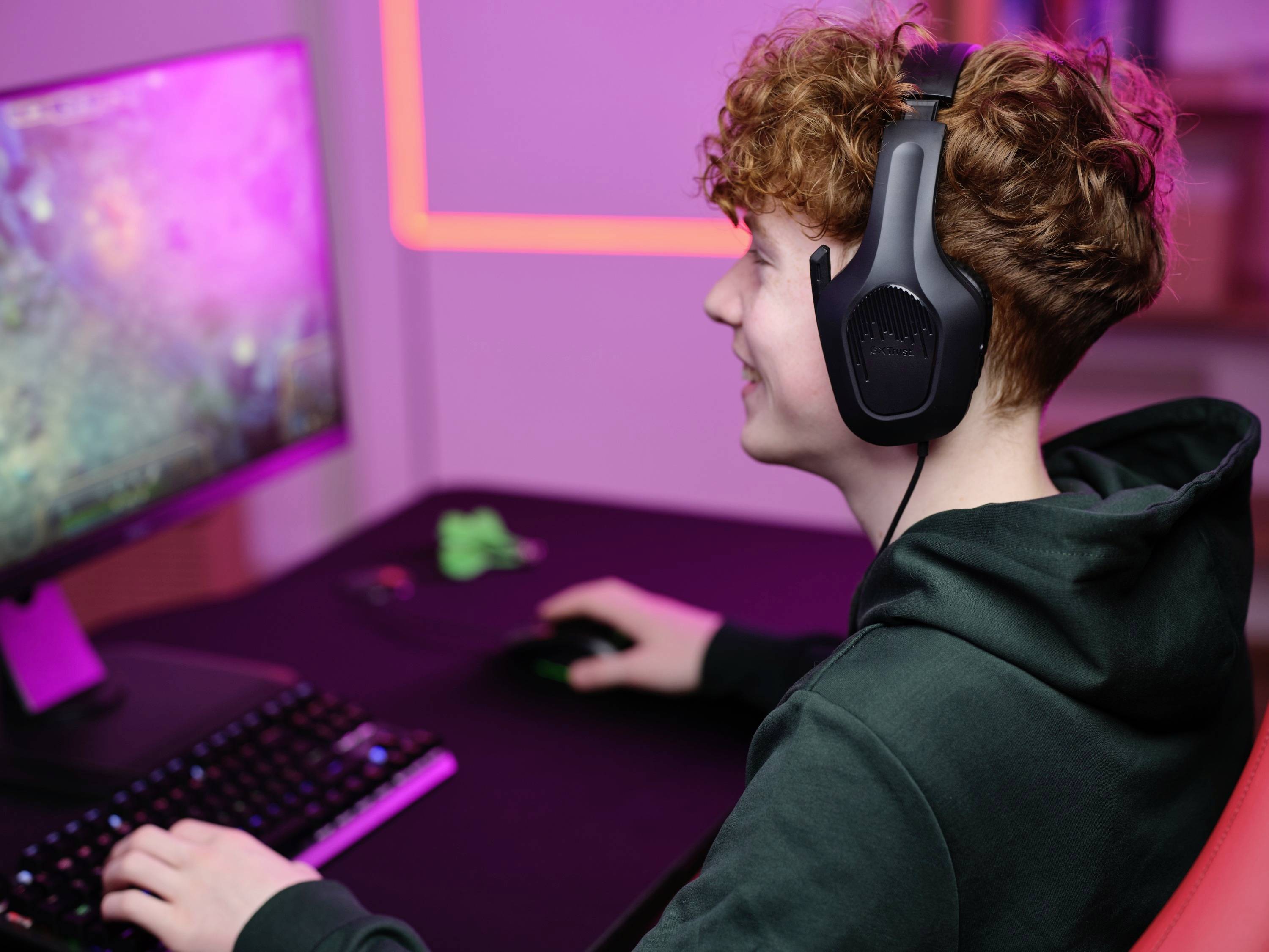 Une personne portant des écouteurs joue sur un ordinateur éclairé par une lumière rose.