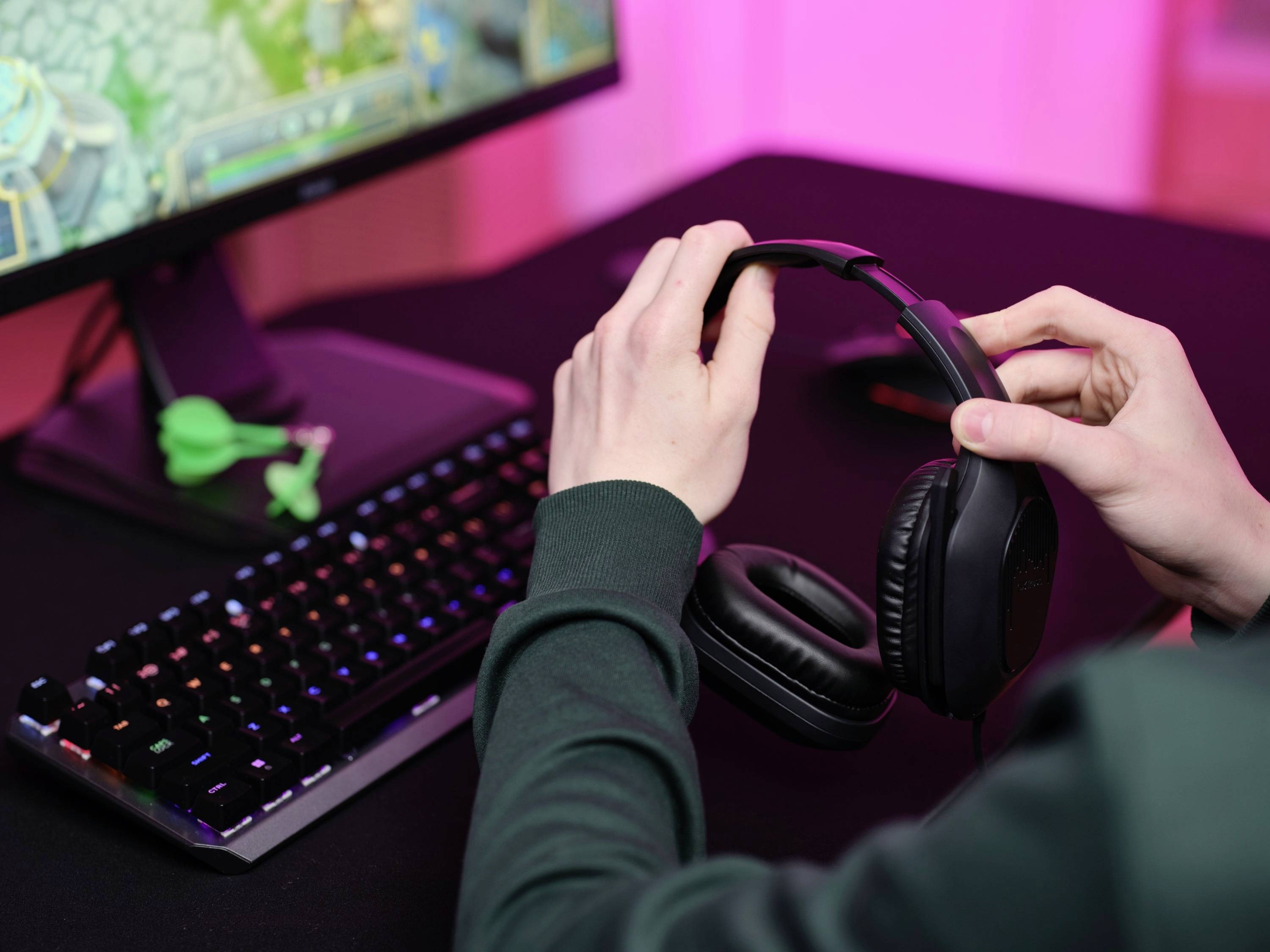 Une personne retire ses écouteurs, un écran d'ordinateur affichant un jeu vidéo apparaît en arrière-plan. Un clavier et une souris sont posés sur la table.