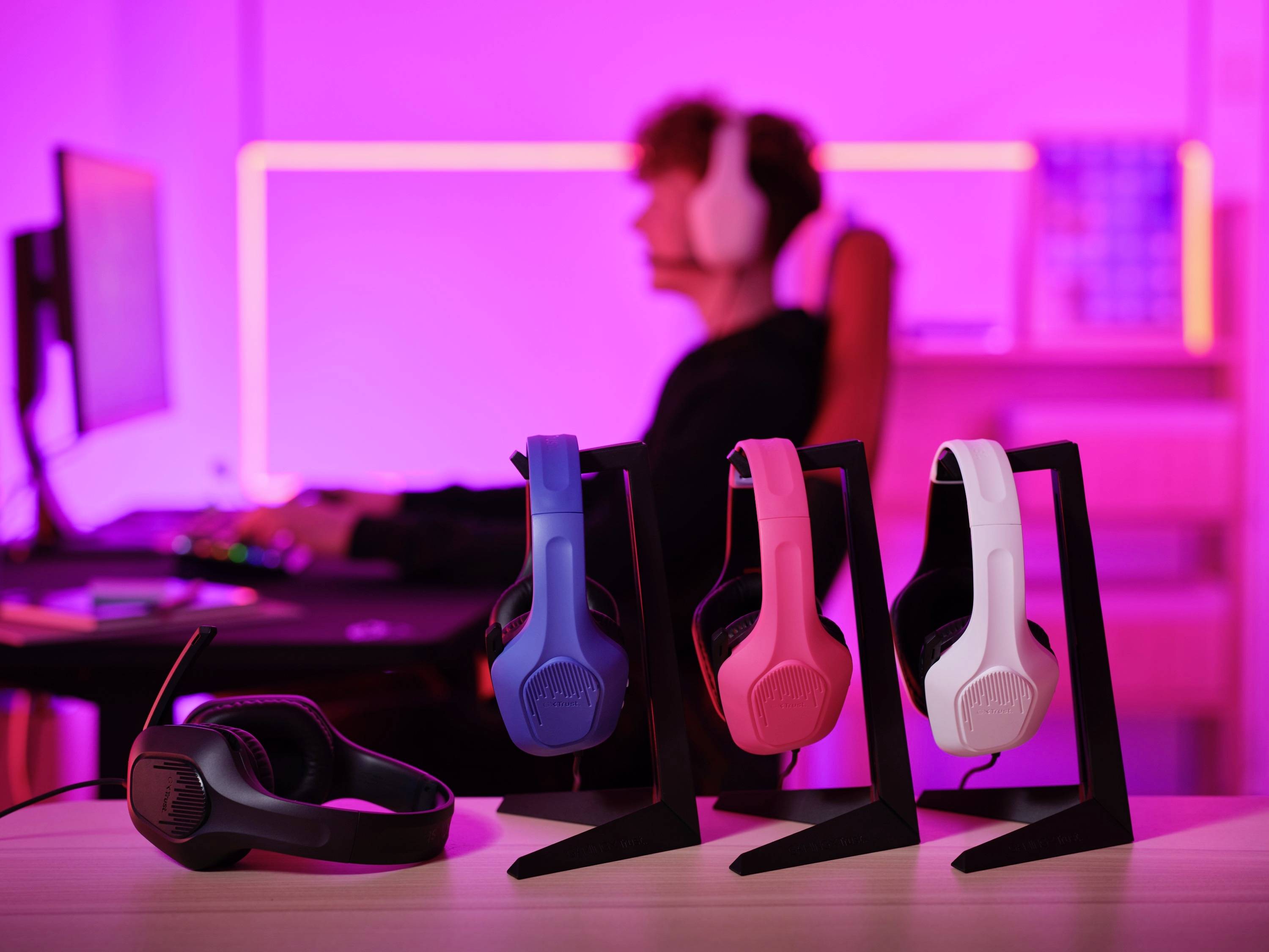 Quatre écouteurs colorés sur des supports devant un arrière-plan flou où une personne est assise devant un ordinateur.