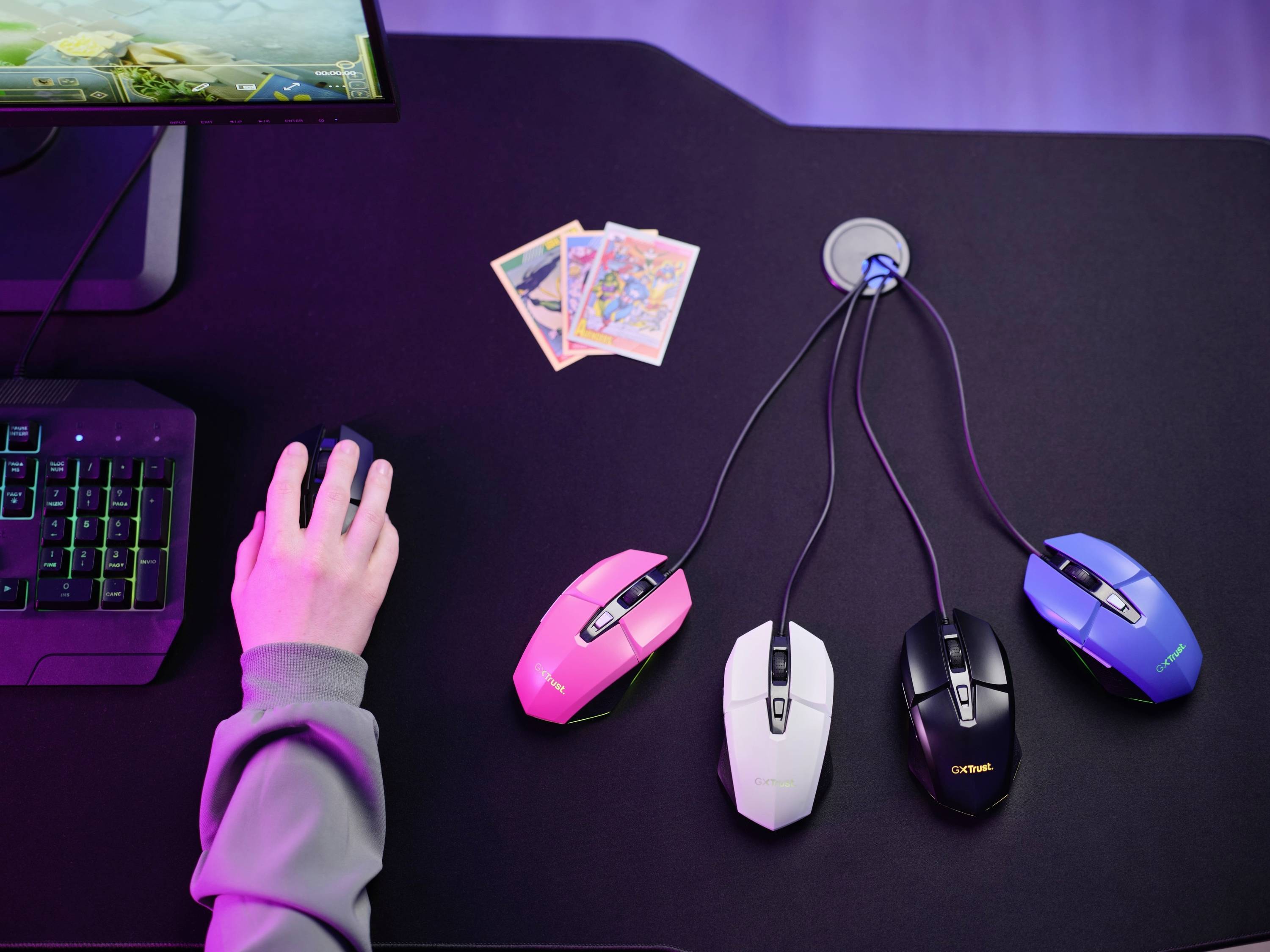 Un bureau avec quatre souris d'ordinateur de couleurs différentes, connectées à un organisateur de câbles. À gauche, une main sur un clavier rétroéclairé.