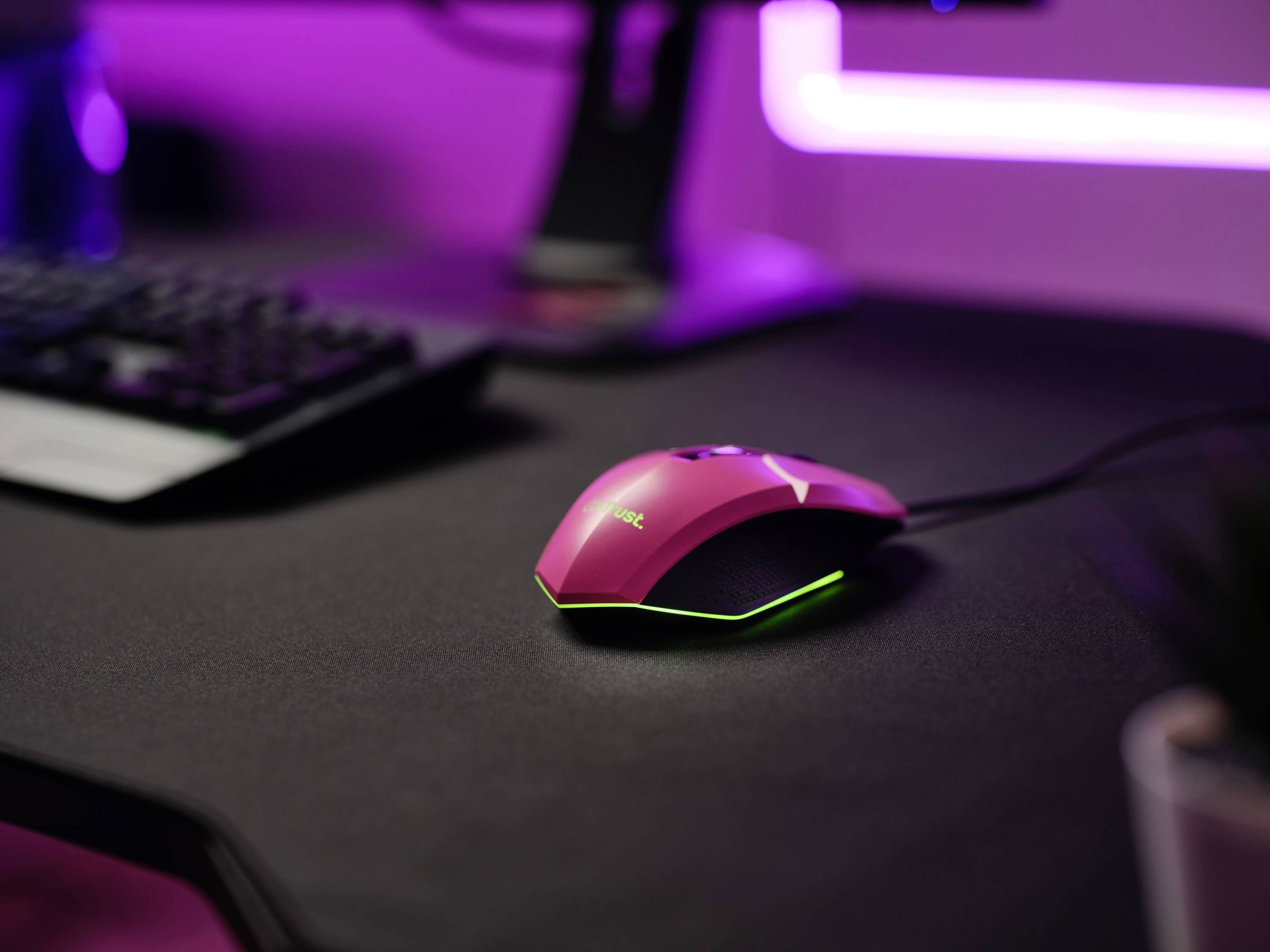 Une souris de gaming rose avec rétroéclairage est posée sur un bureau avec un clavier en arrière-plan, un setup moderne.