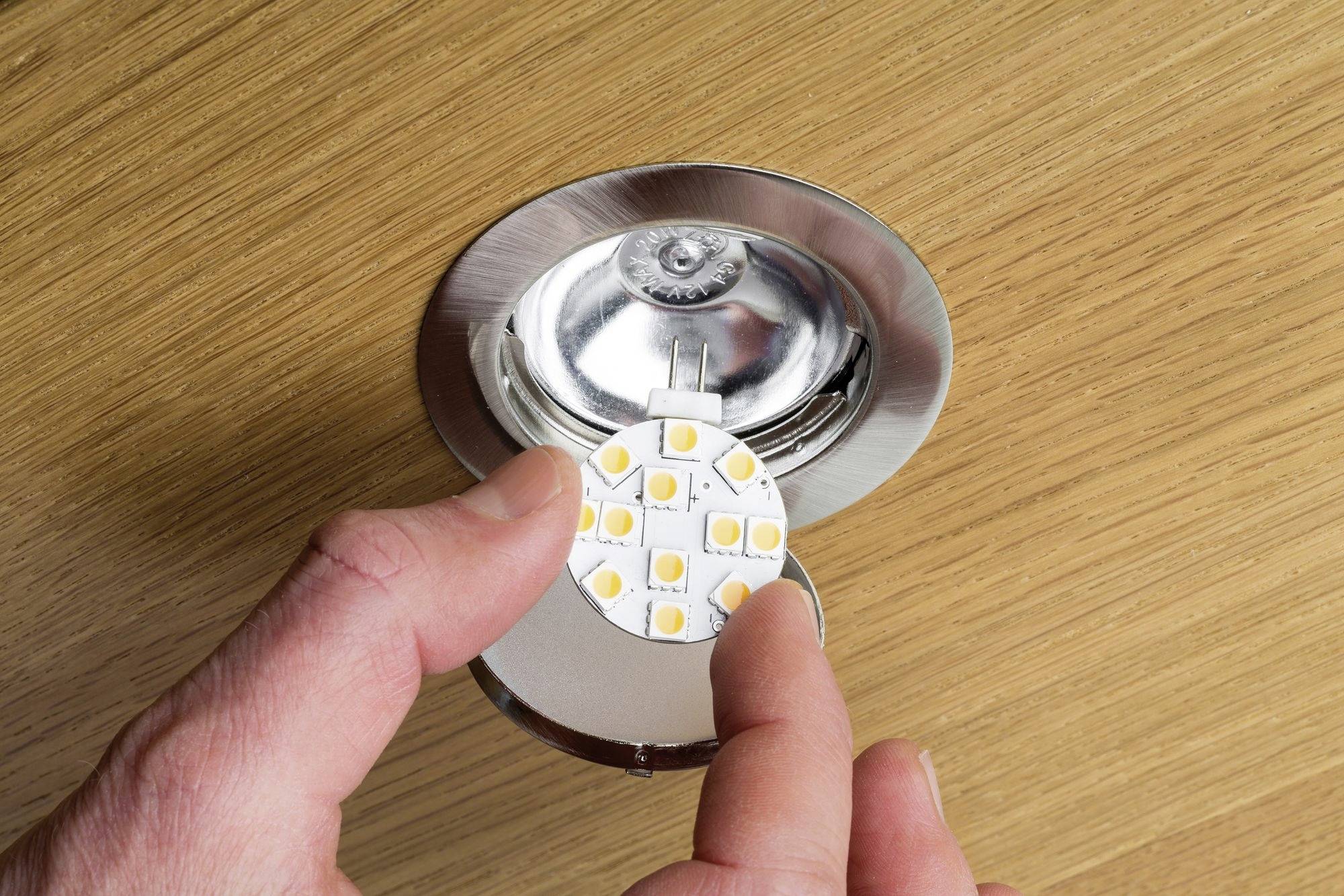 Une personne tient une lampe LED ronde au-dessus d'un luminaire ouvert, prête à être installée sur une surface en bois.