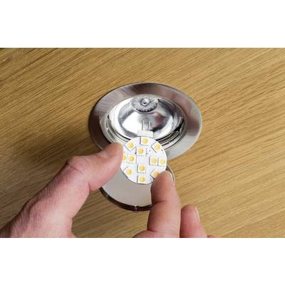Une personne tient une lampe LED ronde au-dessus d'un luminaire ouvert, prête à être installée sur une surface en bois.