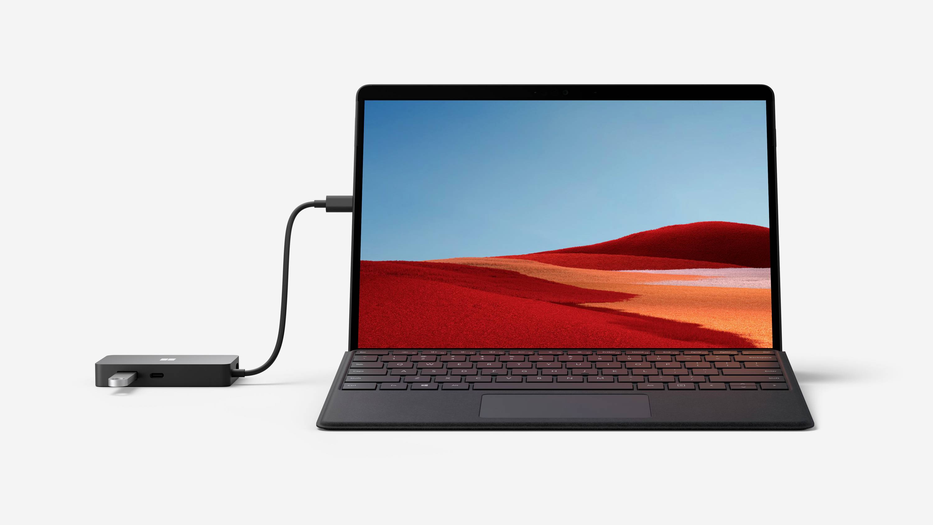 Un ordinateur portable avec un arrière-plan d'écran noir et rouge, connecté à un périphérique externe via un câble sur une surface blanche.