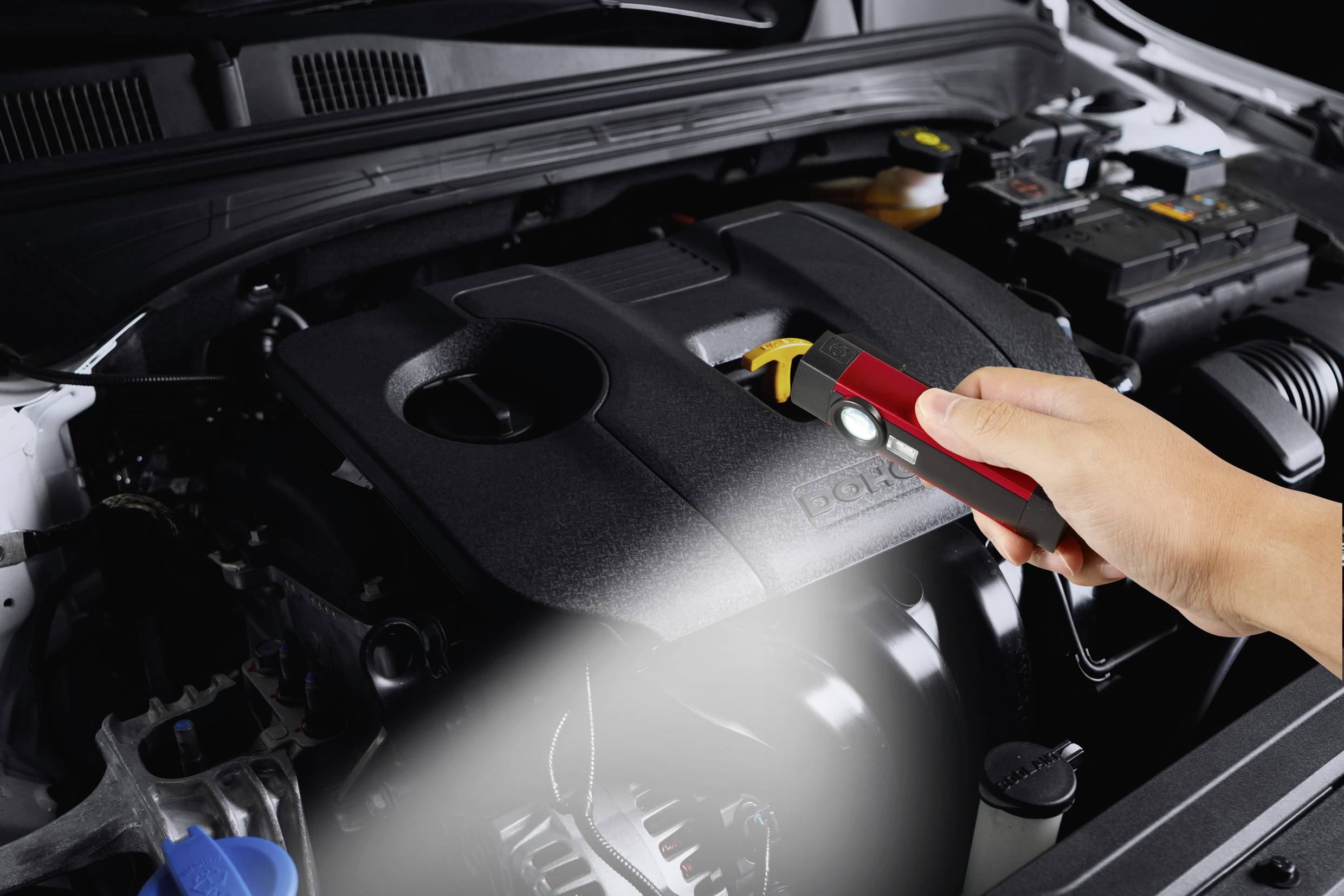 Une personne vérifie le moteur d'une voiture à l'aide d'une lampe de poche. Le capot est ouvert, et l'attention est concentrée sur le bloc moteur.