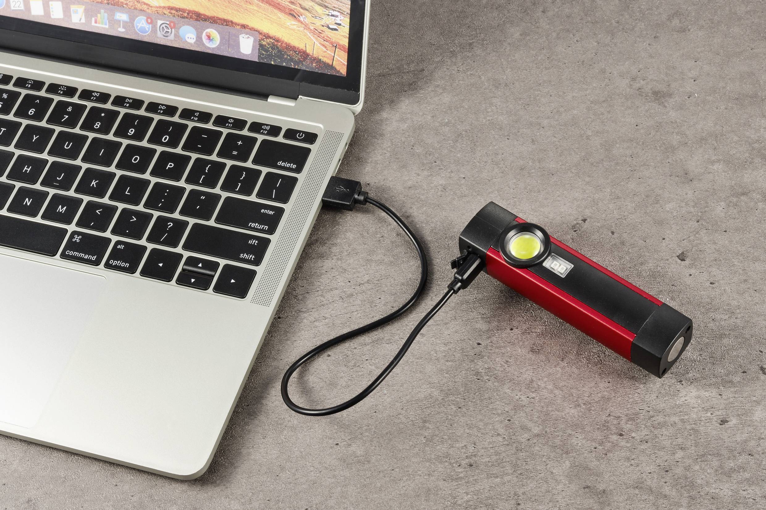 Une lampe de poche rouge est branchée à un ordinateur portable avec un câble USB, posé sur une table.