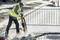 Ouvrier portant un gilet de signalisation jaune et un casque, utilisant un marteau-piqueur pneumatique sur un chantier ; une zone de sécurité et le chantier sont visibles en arrière-plan.