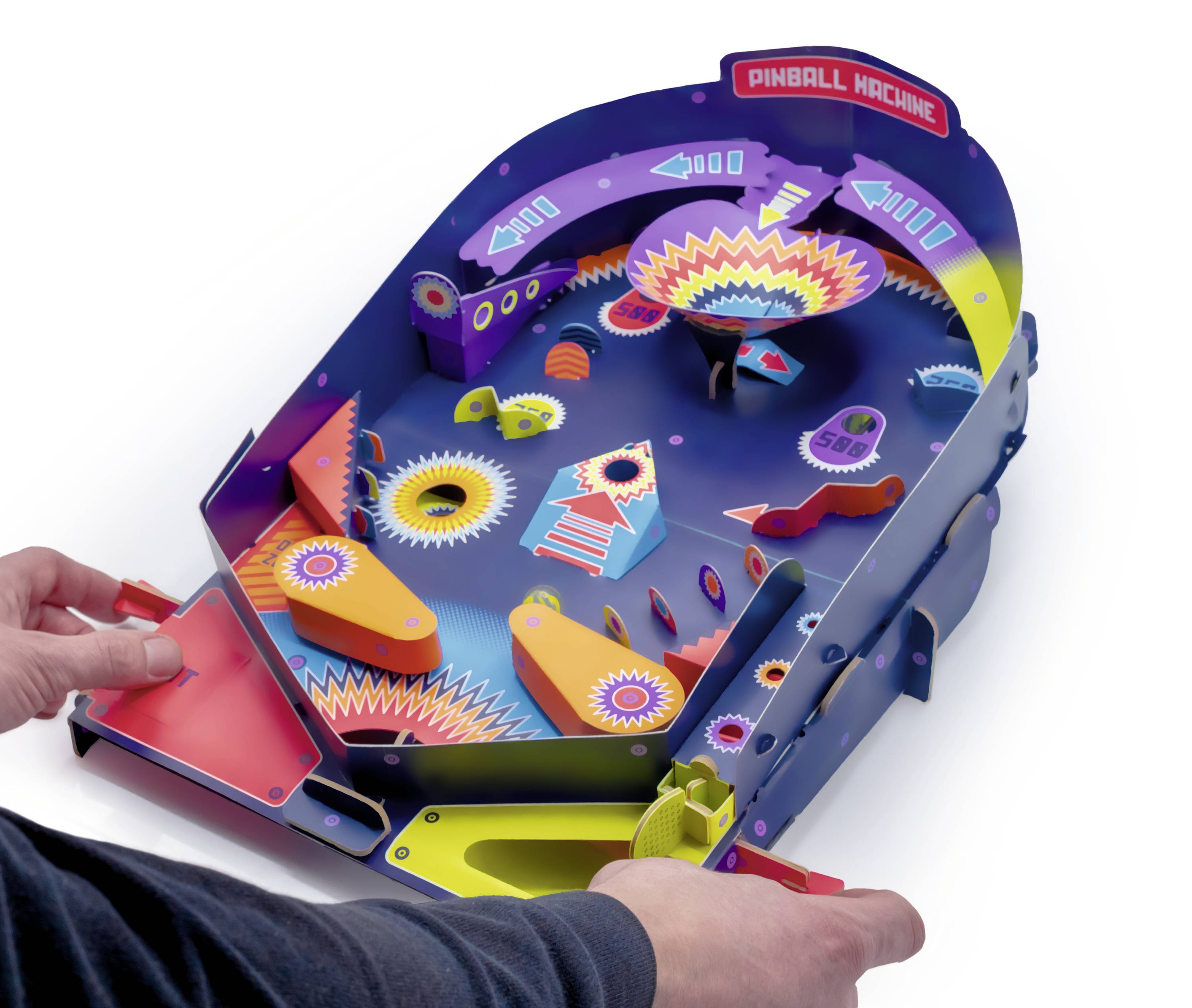 Un flipper de jouet aux couleurs et motifs lumineux est actionné par une paire de mains. La table présente des rampes et des obstacles.