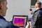 Deux hommes effectuent un diagnostic thermique sur un mur, l'un tenant une tablette avec un affichage coloré, l'autre une caméra.