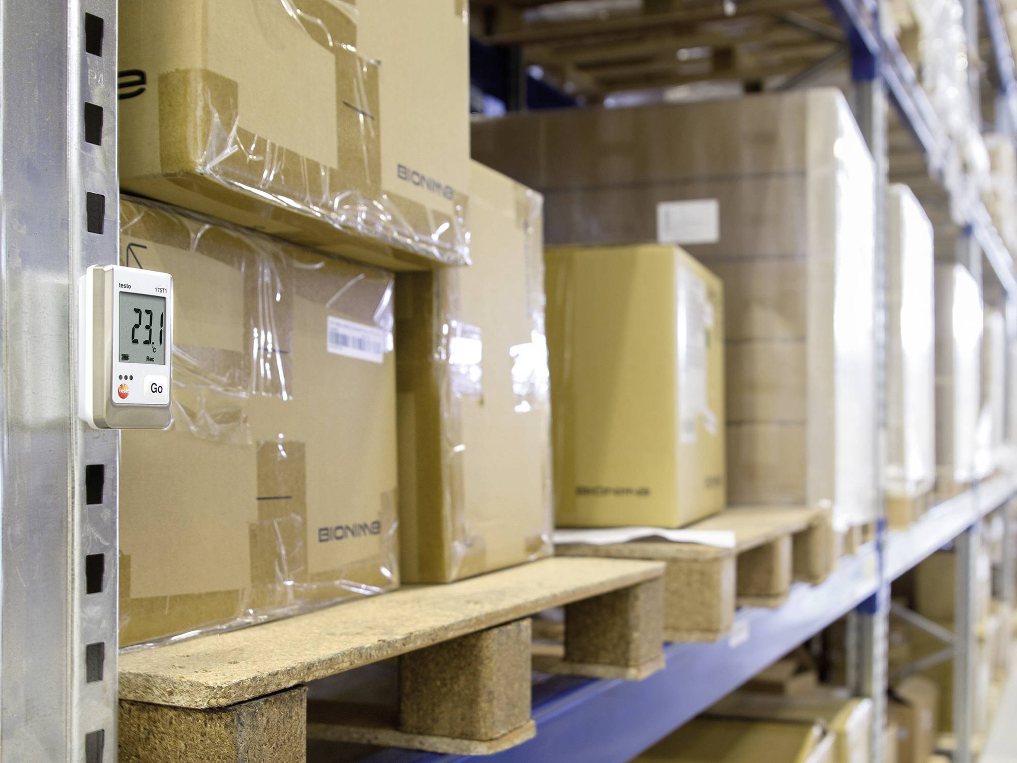 Boîtes en carton sur des étagères de stockage, à côté d'un thermomètre indiquant 23,4 degrés Celsius.