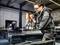 Un homme en tenue de travail utilise une perceuse magnétique sur un poutre en acier dans un atelier. Une autre personne travaille en arrière-plan.