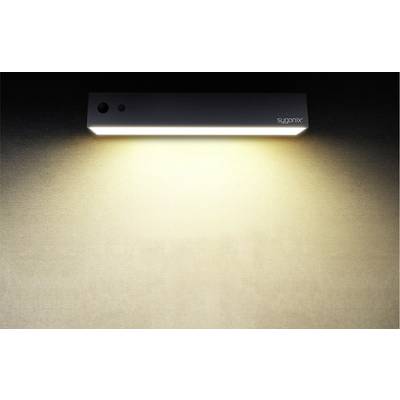 Une lampe murale rectangulaire diffuse une lumière douce et blanc chaud sur un mur beige. Le nom de la marque est dans le coin supérieur droit.