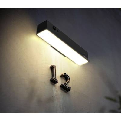 Un luminaire extérieur éclaire le numéro de maison '12' sur un mur au crépuscule.