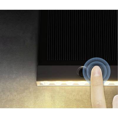 Un doigt touche le bouton d'une lampe solaire qui brille sur son bord inférieur, sur un fond sombre.