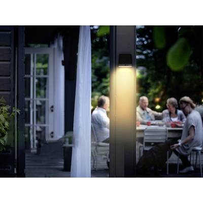 Un groupe de personnes est assis autour d'une table dans un jardin le soir, éclairé par une lampe chaleureuse. Une atmosphère de conversation détendue règne.