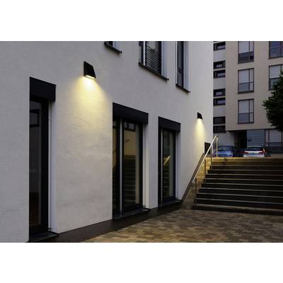 Une vue moderne d'un bâtiment avec un éclairage de soirée sur la façade, un escalier à droite menant à des voitures garées en arrière-plan.